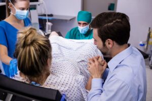 equipo medico examina mujer embarazada parto mientras que hombre sostiene su mano min