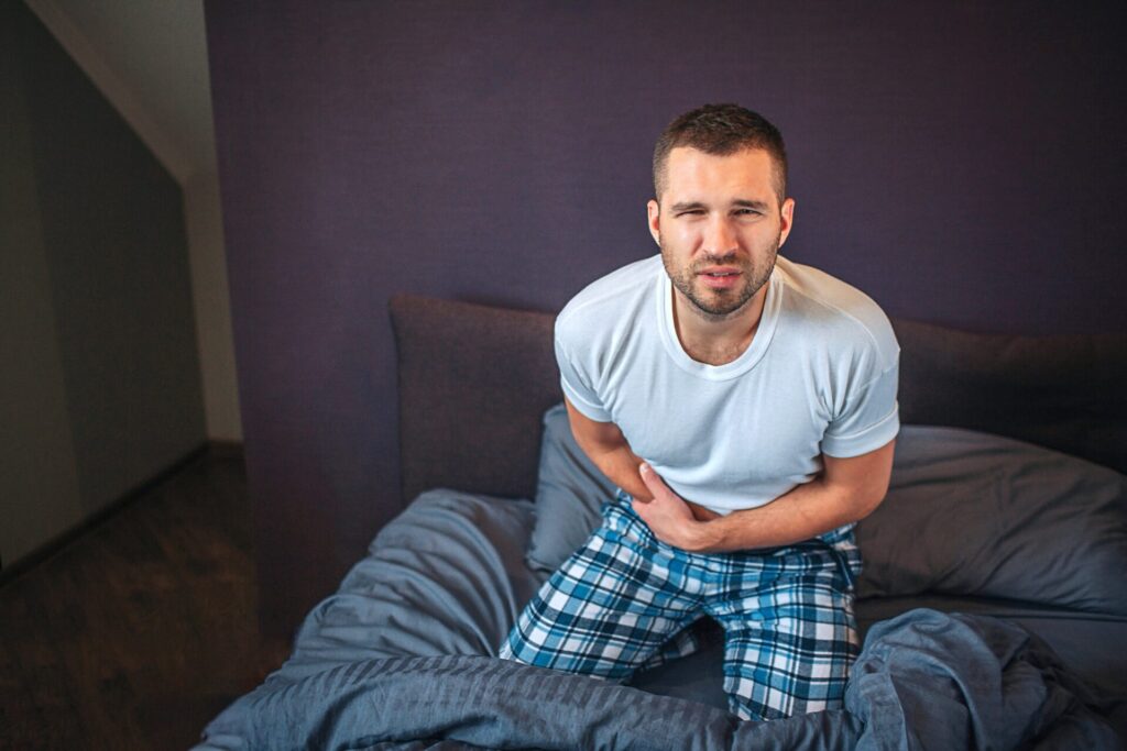 young lightbearded man stands knees bed looks camera he shrinks guy holds hands appendix area he feels pain guy suffer min